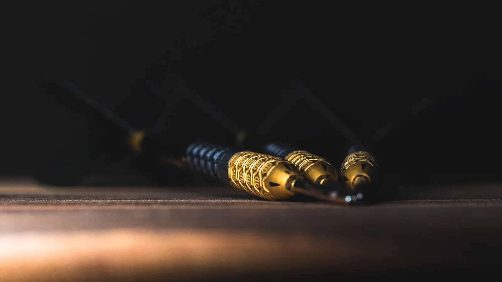 Trois fléchettes à pointe acier posées sur une surface en bois, avec leurs barrels métalliques éclairés de près.